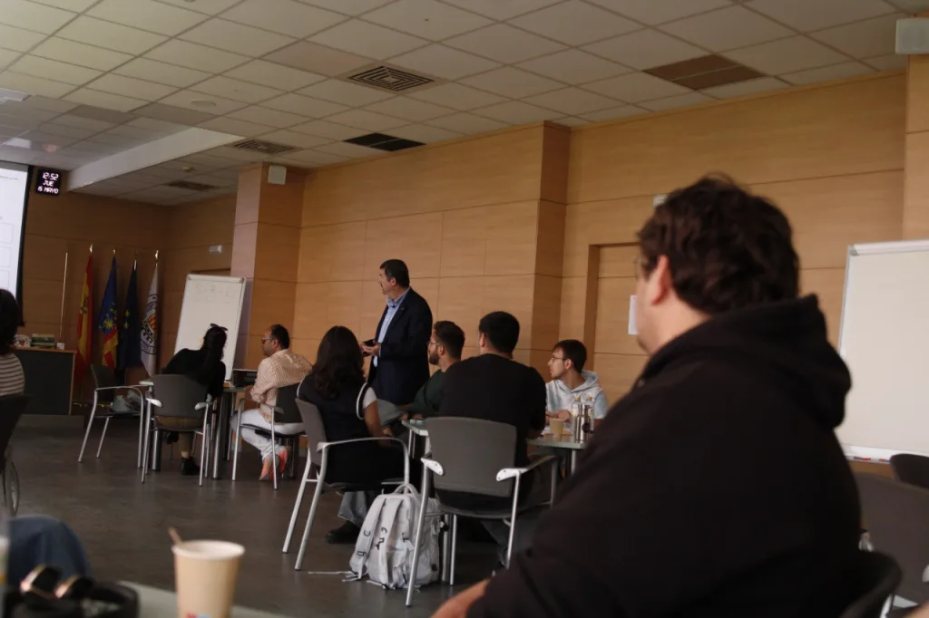 Vista del aula durante el taller: el ponente habla de pie ante los participantes, sentados en grupos