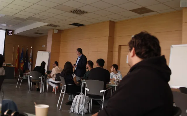 Vista del aula durante el taller: el ponente habla de pie ante los participantes, sentados en grupos