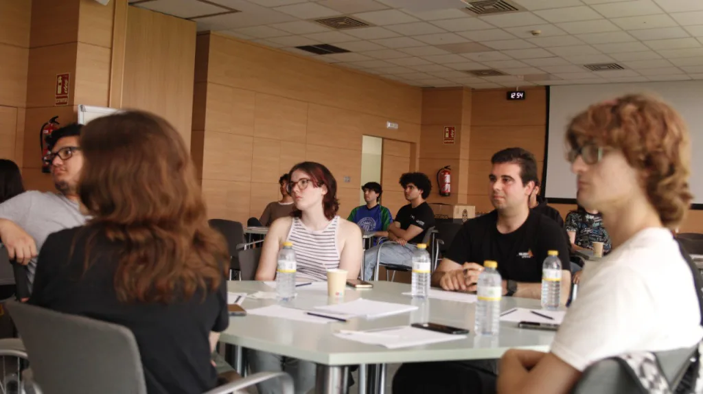 Participantes sentados alrededor de una mesa con botellas de agua y documentos, atentos a la sesión