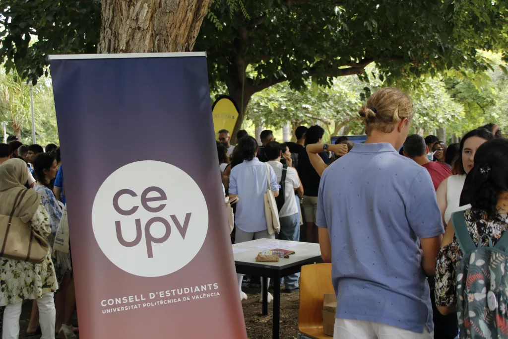 Pancarta del CEUPV junto a un grupo numeroso de estudiantes bajo los árboles, en la jornada de bienvenida