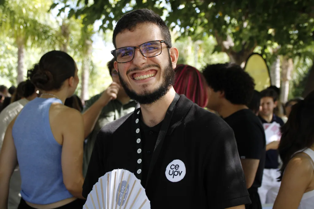 Un miembro del CEUPV, con la camiseta del Consejo y un abanico en la mano, sonríe a la cámara entre los asistentes