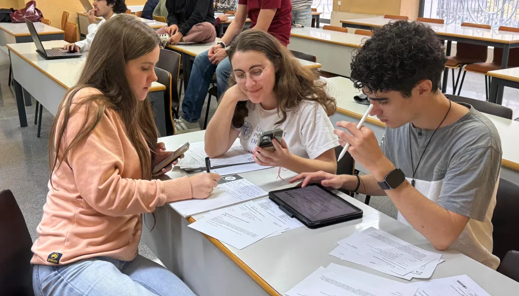 Tres estudiantes trabajan juntos en un caso práctico con documentos impresos, un móvil y una tableta