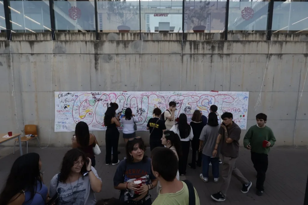Estudiantes escriben y dibujan en el mural colaborativo de la CALUMFEST, una pancarta larga colgada en un muro