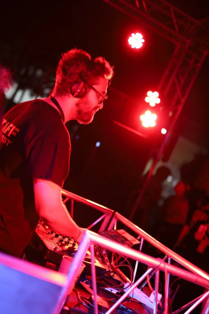 Un DJ con auriculares pincha en la cabina, bajo los focos rojos del escenario