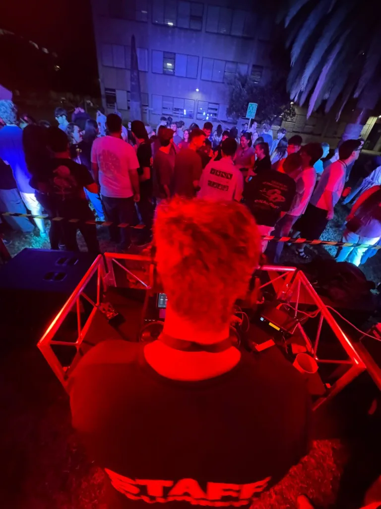 Vista desde la cabina del DJ: una persona de la organización, de espaldas, frente al público que baila de noche
