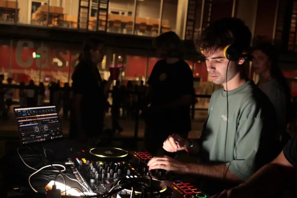 Un DJ con auriculares mezcla con una controladora y un portátil, de noche