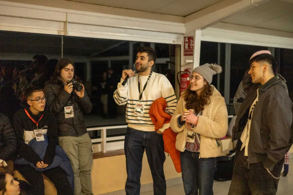 Un miembro de la organización habla con micrófono a los participantes, de noche, bajo un porche