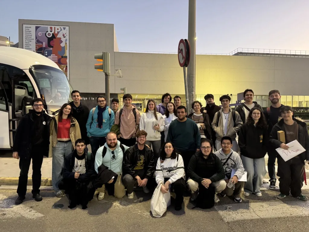 Foto de grupo de los participantes junto al autobús, delante de un edificio de la UPV, al atardecer