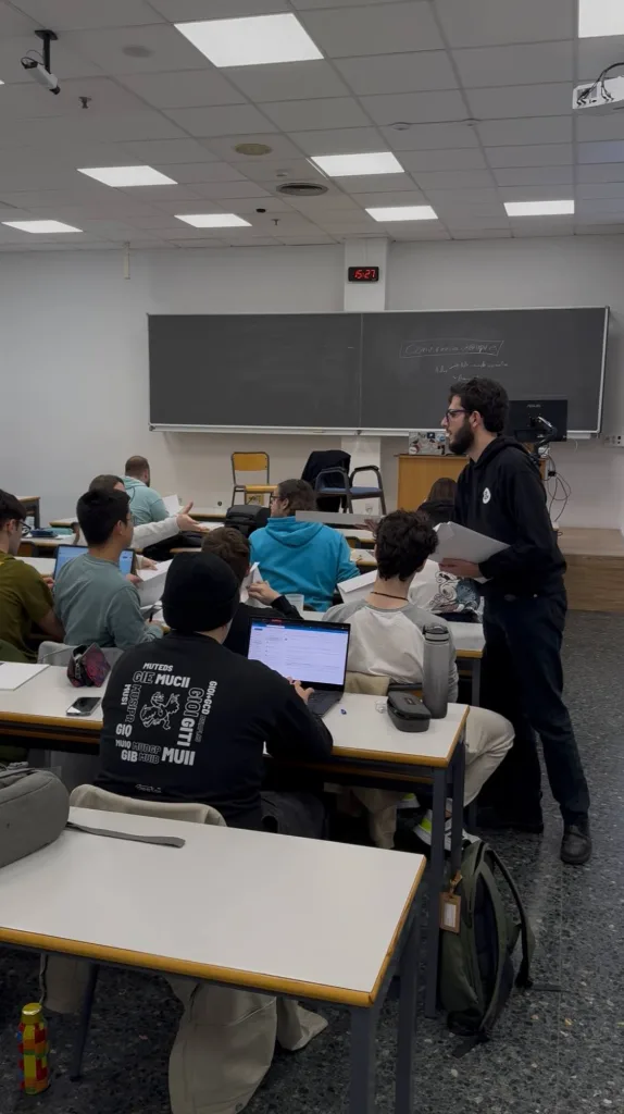 Un formador explica la actividad de pie mientras los participantes trabajan con portátiles en un aula